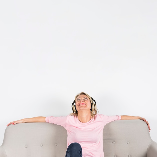 Mature woman sitting on sofa enjoying the music on headphone against white background