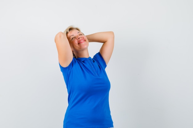 Mature woman in t-shirt holding hands behind head and looking relaxed