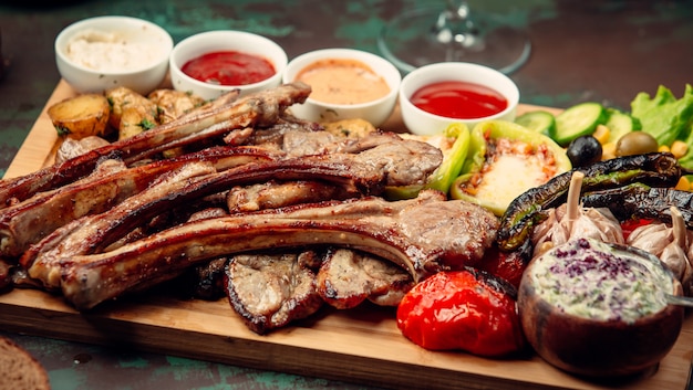 Free Photo meat barbecue with grilled vegetables and variety of sauces on a wooden platter.