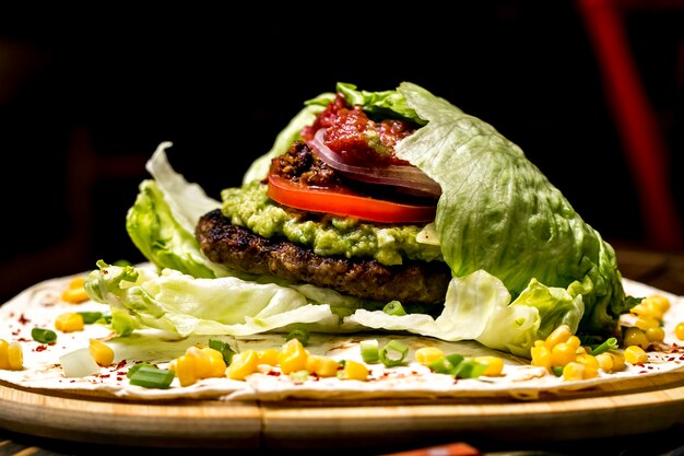 Meat burger in lettuce leaves tomato corns guacamoleside view