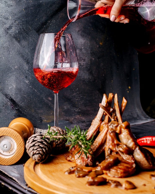 Meat meal on the brown wooden surface along with red wine on the grey surface