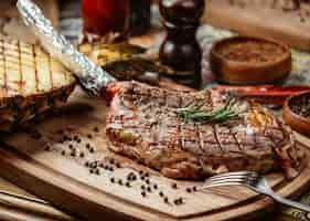 Free photo meat steak on a wooden plate with black pepper and rosemary.