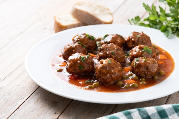 Free photo meatballs green peas and carrot with tomato sauce on wooden table