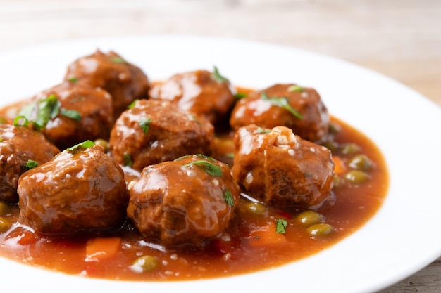 Free photo meatballs green peas and carrot with tomato sauce on wooden table