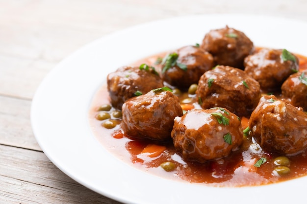 Free photo meatballs green peas and carrot with tomato sauce wooden table