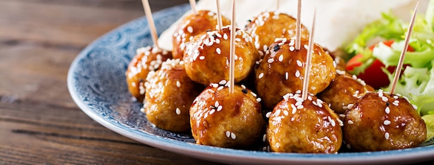 Meatballs in sweet and sour glaze on a plate with pita bread and vegetables in a Moroccan style on a wooden table.