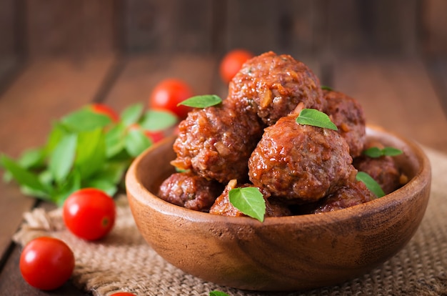 Meatballs in sweet and sour tomato sauce and basil in a wooden bowl