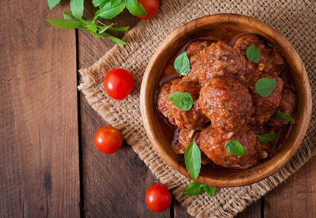 Free photo meatballs in sweet and sour tomato sauce and basil in a wooden bowl