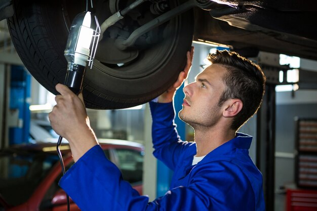 Mechanic examining car tyre using flashlight