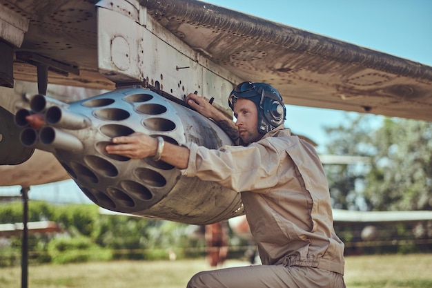 Free photo mechanic in uniform and flying helmet repair old war fighter-interceptor in an open-air museum.