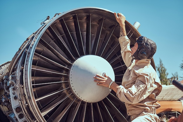 Free photo mechanic in uniform and flying helmet repairing the dismantled airplane turbine in the open air.