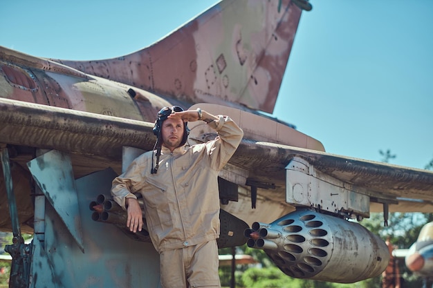 Free photo mechanic in uniform and flying helmet standing near an old war fighter-interceptor in an open-air museum.