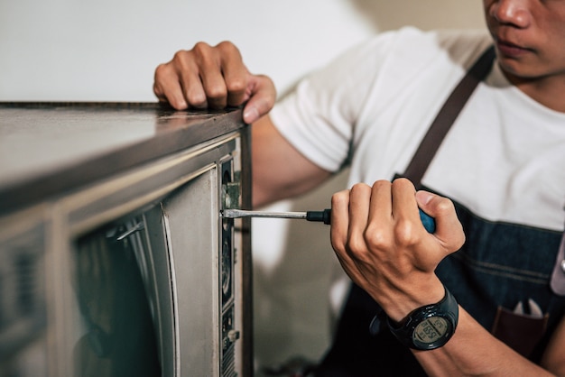 The mechanic uses a screwdriver to tighten the screws on the TV.