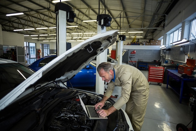 Mechanic using laptop while servicing a car engine