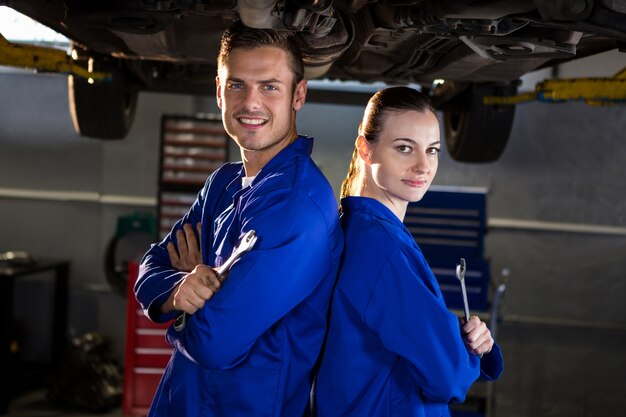 Mechanics standing back to back under a car