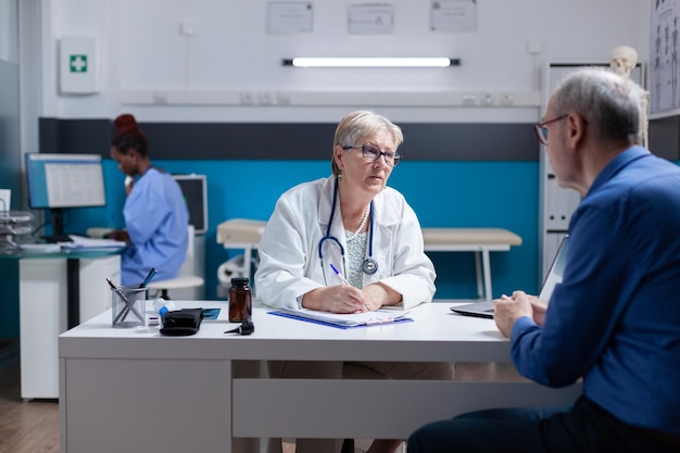 Free Photo medic doing signature on checkup papers to give prescription medicine to patient. woman doctor signing documents after healthcare consultation, giving treatment to senior man with disease.