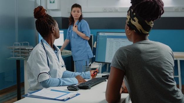 Medic explaining medical information on computer to patient while asking nurse for help in doctors office. Doctor doing healthcare checkup with woman, using monitor and technology