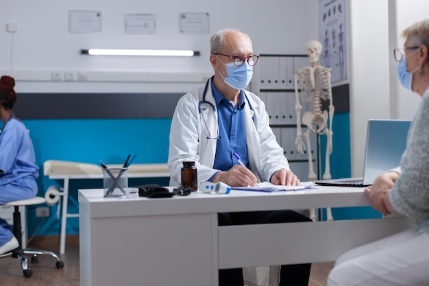 Medic writing on clipboard files while doing consultation with woman during covid 19 pandemic. Physician with face mask preparing prescription document for treatment against disease.