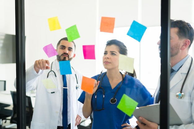 Medical board brainstorming together at the meeting room. Doctors and a nurse writing memos on sticky notes