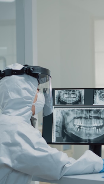 Free Photo medical dentistry staff with ppe suits using modern technology while consulting patient with oral care issues. stomatologist and dental nurse looking at teeth animation model for implant