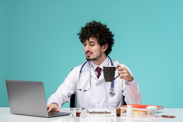 Medical in lab coat young serious handsome doctor working on computer holding black coffee cup