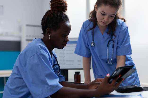 Free Photo medical nurses analyzing disease symptoms discussing healthcare treatment working in hospital office. teamworks checking pharmaceutical medication on tablet computer sitting at desk