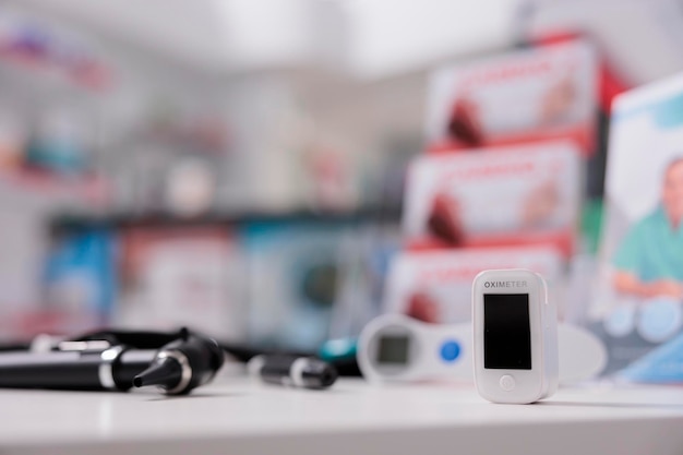 Free photo medical oximeter standing on table in empty drugstore ready to be used by client, digital device to measure oxygen saturation. pharmacy filled with medicaments, vitamins and pharmaceutical products