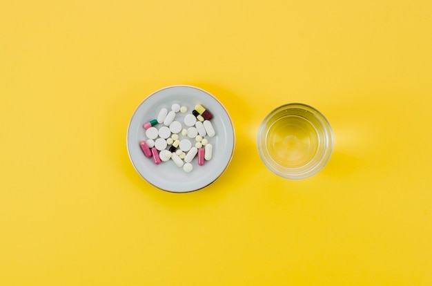 Free photo medical pills in bowl and glass water on yellow background