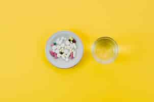 Free photo medical pills in bowl and glass water on yellow background