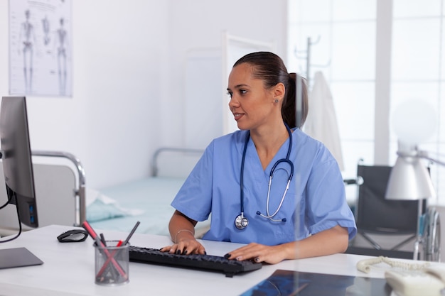 Medical practitioner using computer in hospital office. Health care physician using computer in modern clinic looking at monitor, medicine, profession, scrubs.