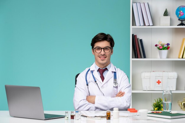 Medical smart young doctor in lab coat working remotely on computer crossing hands