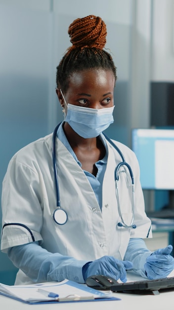 Medical specialist discussing healing treatment with ill woman in doctors office. Doctor doing medical consultation with patient while wearing face masks for protection against pandemic