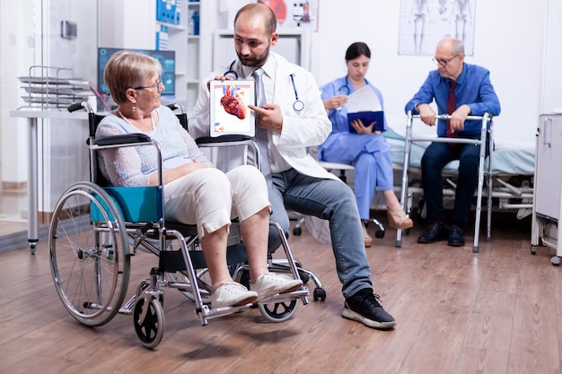 Medical stuff presenting a booklet with arrhythmias to handicapped senior woman sitting in wheelchair