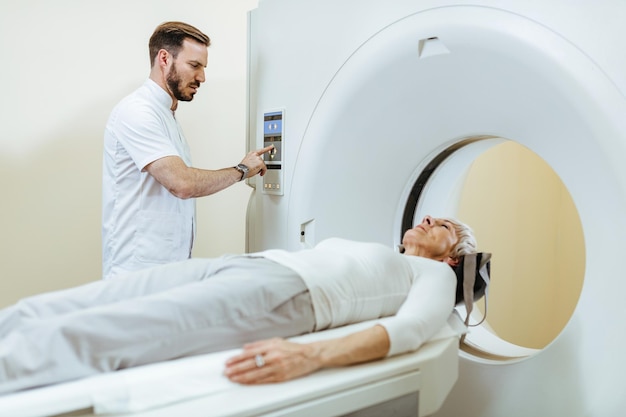 Medical technician starting MRI scan procedure of mature patient in examination room