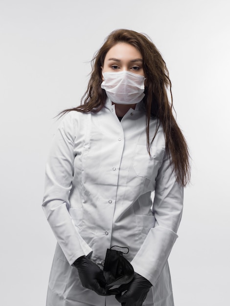 Free photo medical worker in white doctor uniform with protective mask holding black mask in her hands