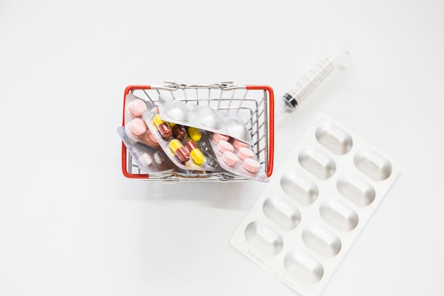 Free photo medicine pills pack in miniature shopping cart with syringe on white background