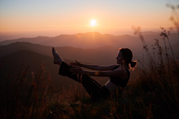 Meditating female is sitting on grass in mountains