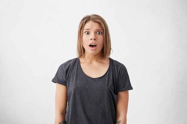 Medium close-up of frightened excited woman with trendy hairstyle looking with big eyes and opened mouth being surprised to see someone.