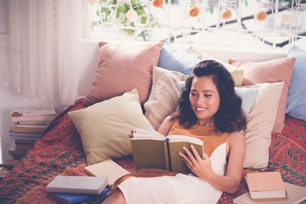 Medium closeup of young woman reading a book in her bed