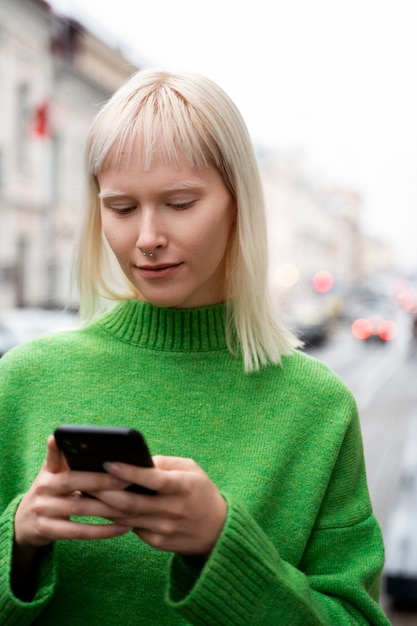 Free photo medium shot albino woman holding smartphone