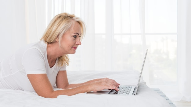 Medium shot blonde woman in bed with laptop