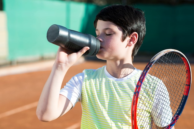 medium shot brunette kid drinking water with racket on the shoulder