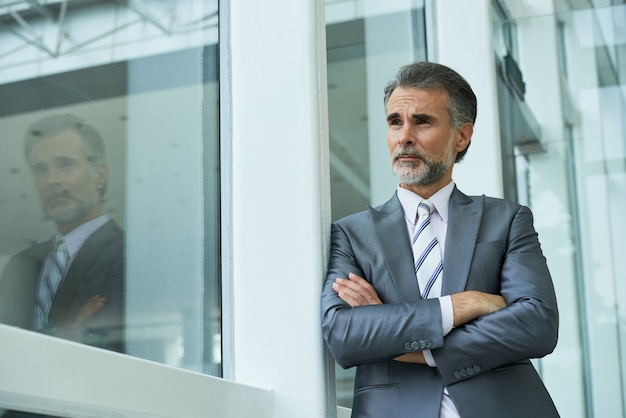 Medium shot of businessman standing with arms folded leaning on the window frame