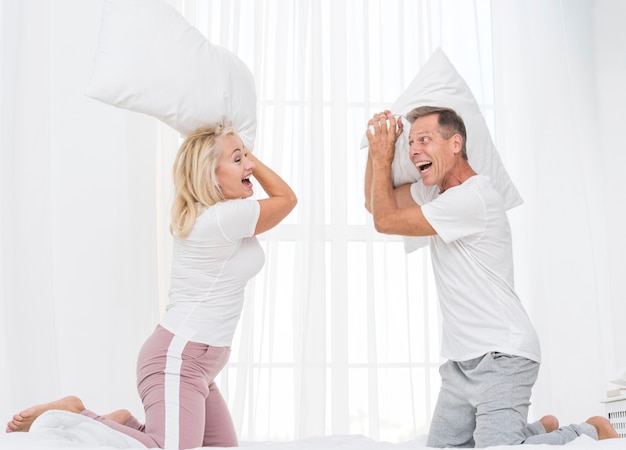 Free photo medium shot couple having a pillow fight