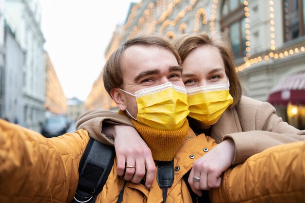 Medium shot couple with masks taking selfie