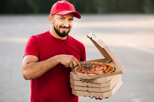 Medium shot delivery guy slicing pizza