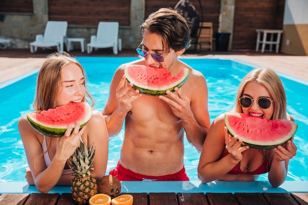 Free photo medium shot friends eating watermelon in pool