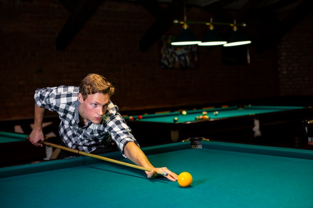 Medium shot guy with pool cue hitting yellow ball