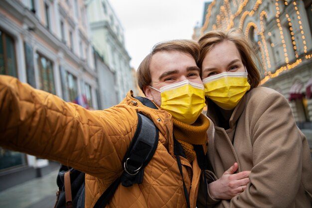 Medium shot happy couple with masks taking selfie