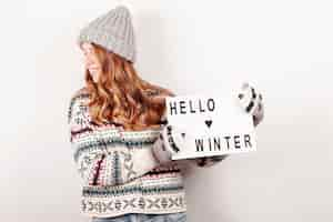 Free photo medium shot happy girl holding hello winter sign